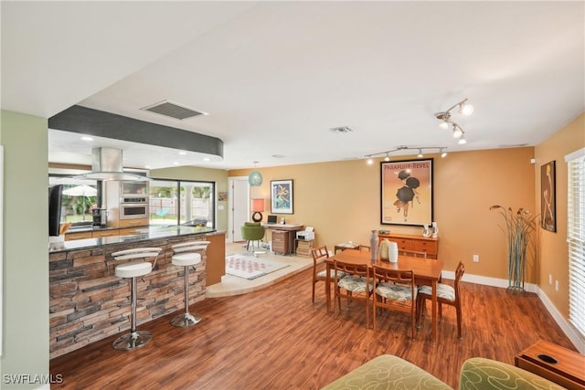 dining area with baseboards, track lighting, visible vents, and wood finished floors