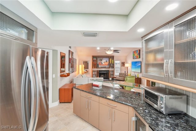 kitchen with visible vents, a ceiling fan, dark stone countertops, freestanding refrigerator, and a fireplace