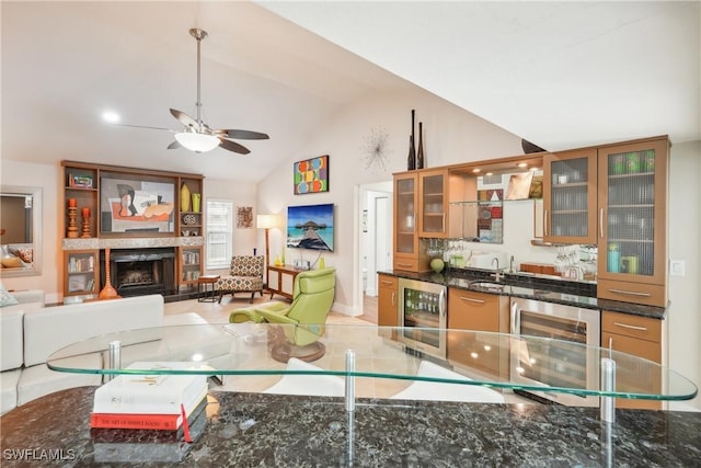 kitchen with wine cooler, a fireplace with raised hearth, glass insert cabinets, vaulted ceiling, and dark stone counters