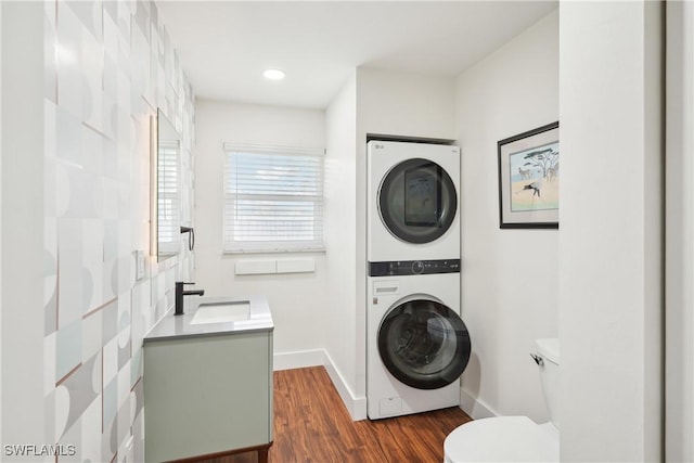 laundry area with stacked washer and dryer, laundry area, dark wood-style flooring, a sink, and baseboards