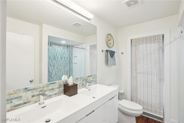 bathroom with a tile shower, tasteful backsplash, a sink, and visible vents