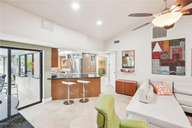 kitchen with a peninsula, a breakfast bar, visible vents, vaulted ceiling, and freestanding refrigerator