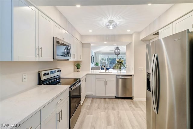 kitchen with a sink, light wood-style floors, white cabinets, light countertops, and appliances with stainless steel finishes