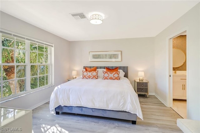 bedroom with ensuite bathroom, light wood finished floors, visible vents, and baseboards