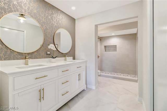 bathroom with a sink, marble finish floor, tiled shower, double vanity, and wallpapered walls