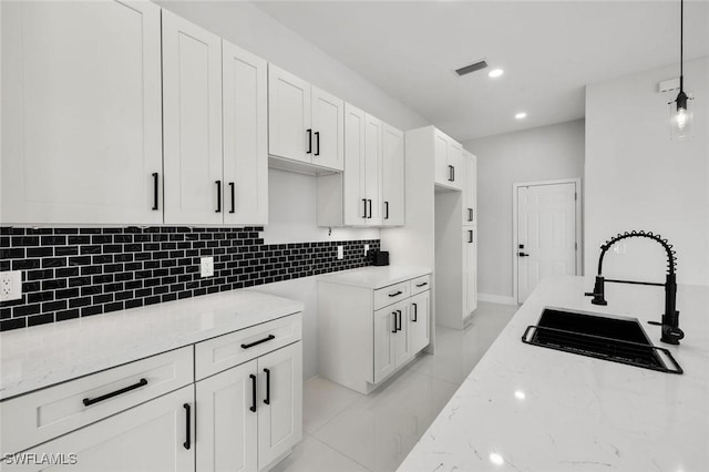 kitchen with visible vents, decorative backsplash, white cabinets, light stone counters, and a sink