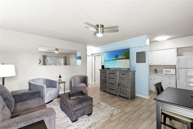 living area with a textured ceiling, light wood finished floors, a ceiling fan, and baseboards