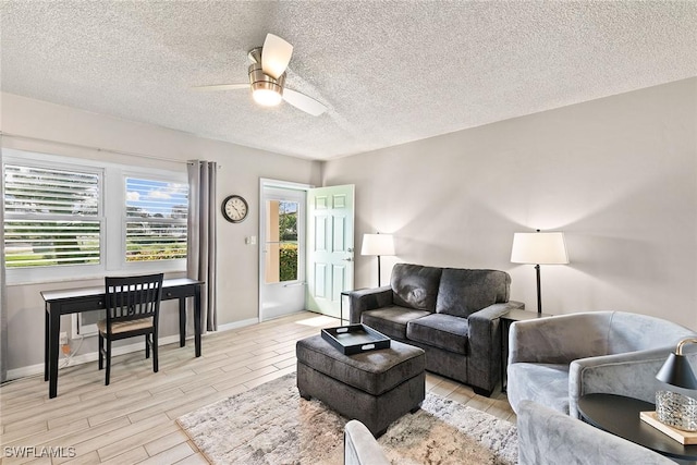 living area featuring baseboards, ceiling fan, light wood-style flooring, and a textured ceiling