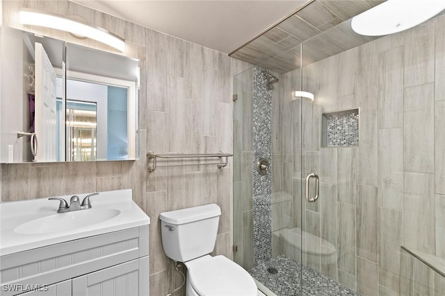 bathroom with a shower stall, vanity, toilet, and tile walls