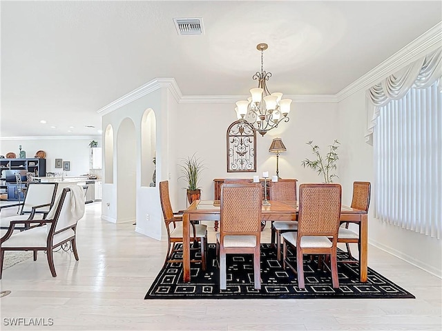 dining room with arched walkways, visible vents, light wood finished floors, and ornamental molding