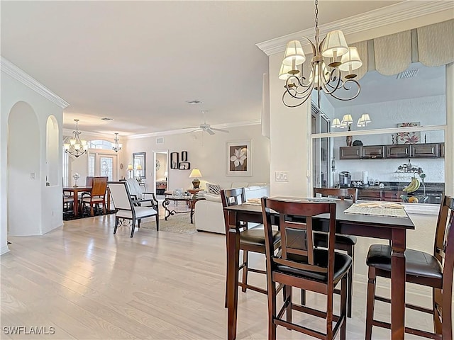 dining space with arched walkways, light wood-style flooring, crown molding, and ceiling fan with notable chandelier