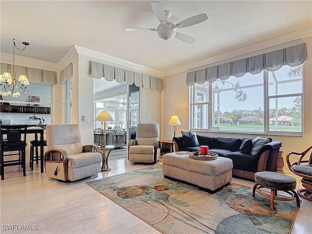 living room featuring a healthy amount of sunlight, wood finished floors, crown molding, and ceiling fan with notable chandelier