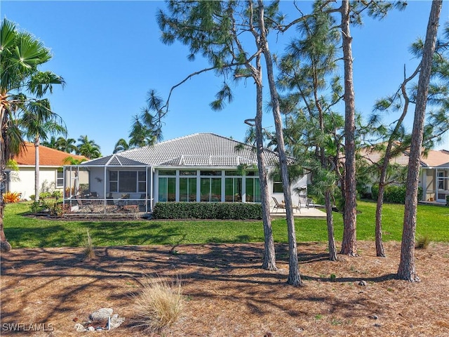 rear view of house featuring glass enclosure, a yard, and a tile roof