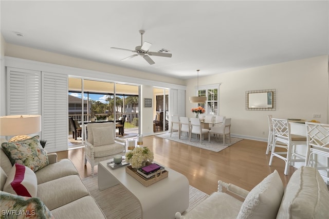 living area with a ceiling fan, wood finished floors, a wealth of natural light, and baseboards