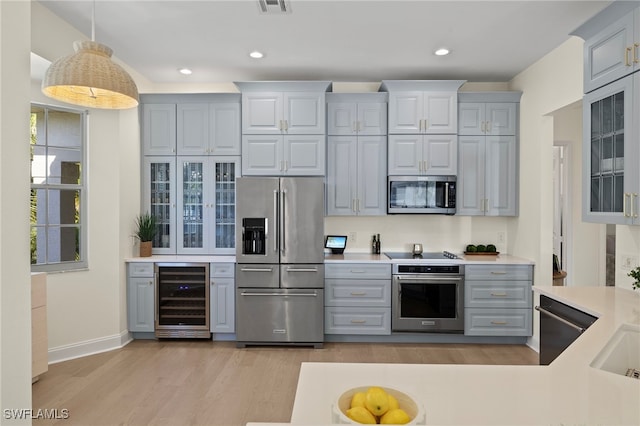 kitchen with beverage cooler, light countertops, appliances with stainless steel finishes, gray cabinets, and glass insert cabinets