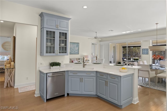 kitchen featuring a peninsula, a sink, light wood-style floors, gray cabinets, and dishwasher