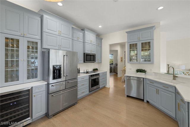 kitchen with wine cooler, stainless steel appliances, gray cabinets, a sink, and light wood-type flooring