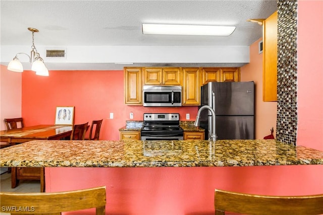 kitchen with visible vents, appliances with stainless steel finishes, dark stone countertops, a textured ceiling, and a kitchen bar