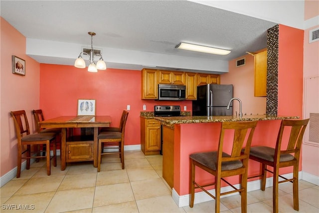 kitchen with a breakfast bar, brown cabinets, stainless steel appliances, visible vents, and a peninsula