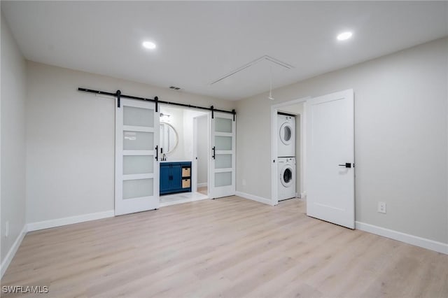 spare room with stacked washer and clothes dryer, light wood-style flooring, a barn door, attic access, and baseboards