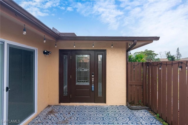 view of exterior entry featuring fence and stucco siding