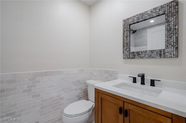 bathroom featuring toilet, a wainscoted wall, tile walls, and vanity