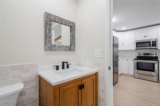 bathroom featuring toilet, vanity, wood finished floors, and tile walls