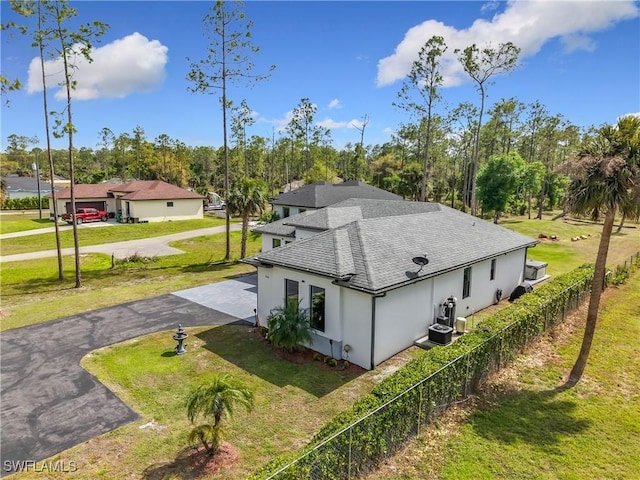 view of home's exterior featuring cooling unit, fence, roof with shingles, a yard, and aphalt driveway