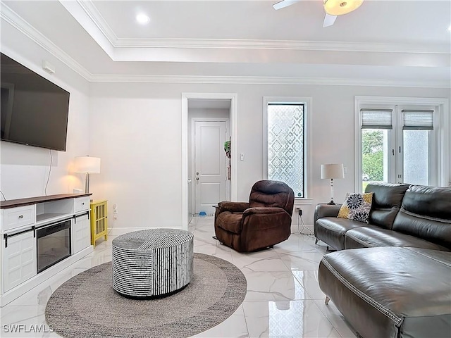 living area with marble finish floor, a tray ceiling, a glass covered fireplace, crown molding, and baseboards