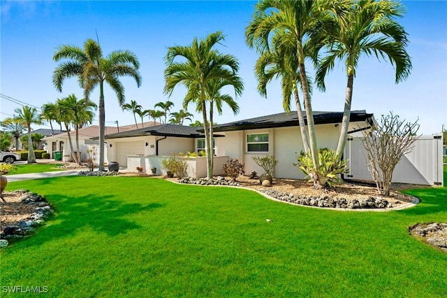 ranch-style home featuring a front lawn, an attached garage, fence, and stucco siding