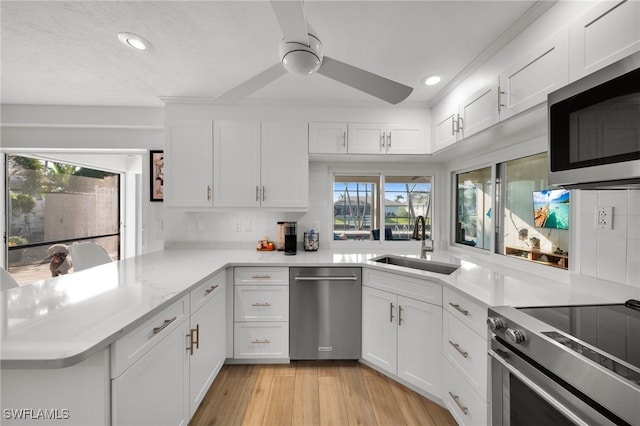 kitchen with stainless steel appliances, a peninsula, a sink, white cabinetry, and light countertops