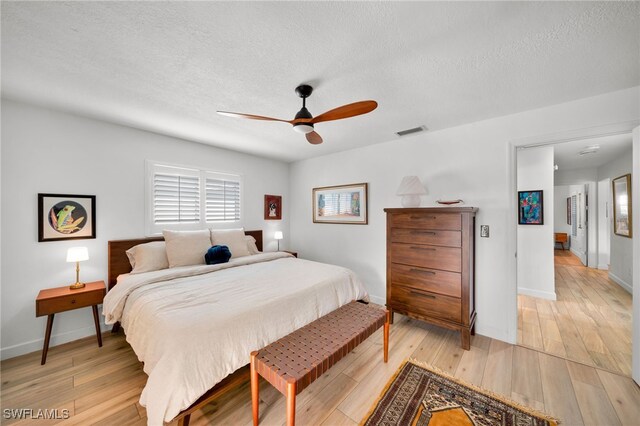 bedroom featuring baseboards, light wood-style flooring, visible vents, and a textured ceiling