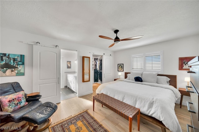 bedroom featuring a textured ceiling, a barn door, a walk in closet, and light wood-style floors