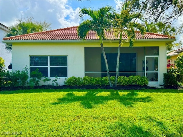 rear view of house featuring a sunroom, a tile roof, a yard, and stucco siding