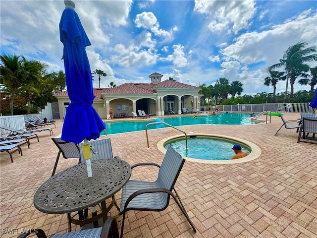 community pool with a patio, fence, and a hot tub