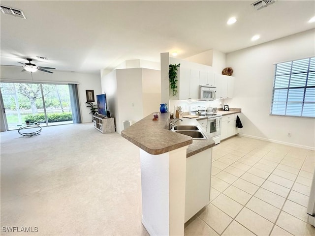 kitchen featuring visible vents, white cabinets, a sink, white appliances, and a peninsula