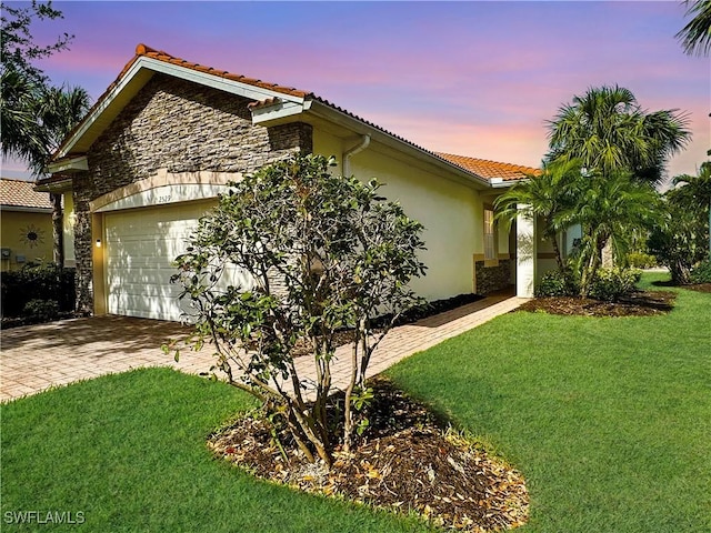 property exterior at dusk with a garage, a lawn, a tiled roof, and stucco siding