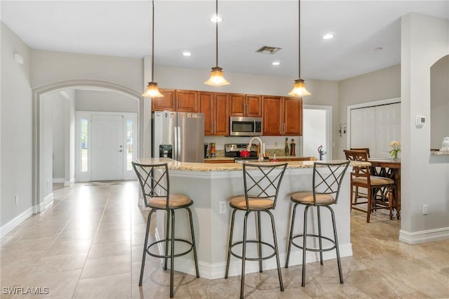 kitchen with arched walkways, a center island with sink, stainless steel appliances, visible vents, and brown cabinetry