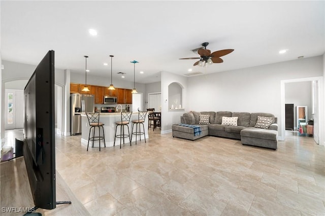 living room featuring a ceiling fan, arched walkways, baseboards, and recessed lighting