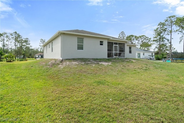 back of house featuring a trampoline, a sunroom, a yard, and stucco siding