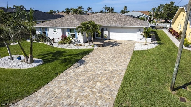 single story home with a front lawn, decorative driveway, a shingled roof, and an attached garage