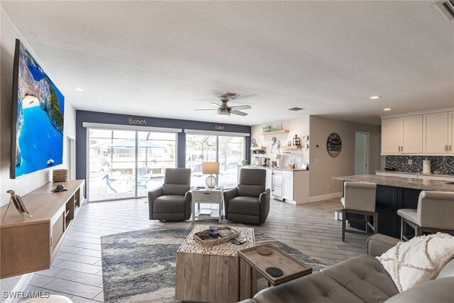 living room with ceiling fan, baseboards, and a textured ceiling