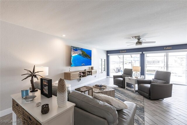 living area with a textured ceiling, ceiling fan, wood finished floors, visible vents, and baseboards