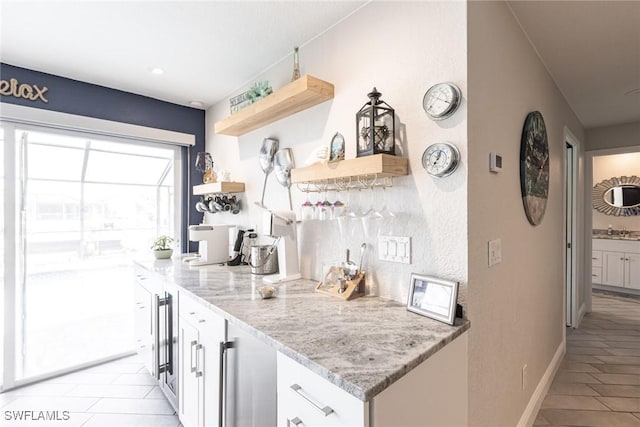 kitchen with baseboards, white cabinets, light stone countertops, open shelves, and a sink