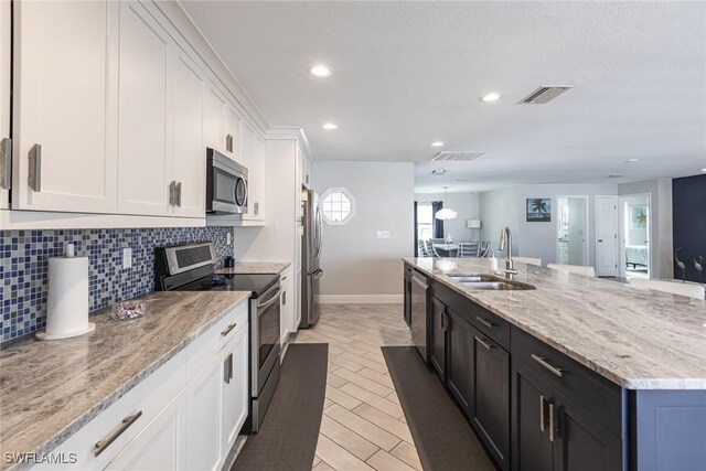 kitchen with visible vents, white cabinets, light stone counters, stainless steel appliances, and a sink