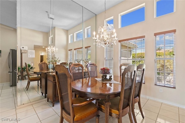 dining space featuring a towering ceiling, an inviting chandelier, light tile patterned floors, and baseboards