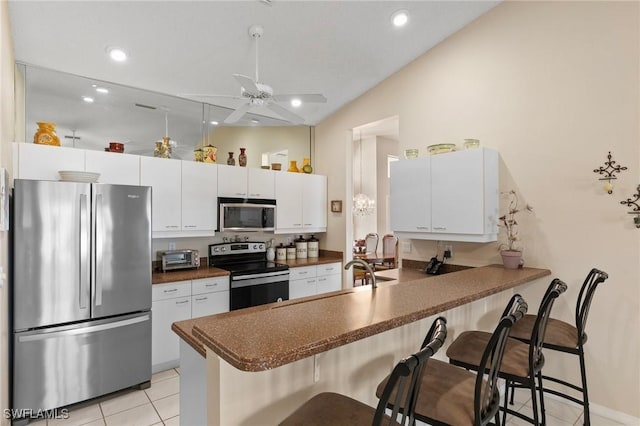 kitchen with a breakfast bar, dark countertops, appliances with stainless steel finishes, white cabinetry, and a peninsula