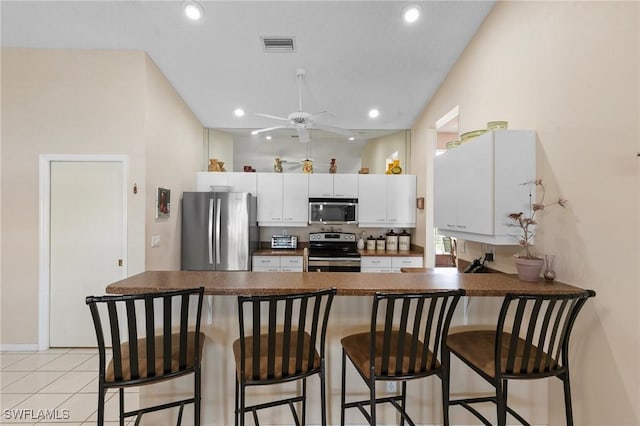 kitchen featuring a breakfast bar area, dark countertops, visible vents, appliances with stainless steel finishes, and a peninsula