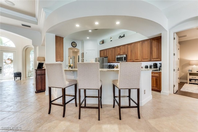 kitchen featuring stainless steel appliances, brown cabinetry, ornamental molding, and a kitchen bar