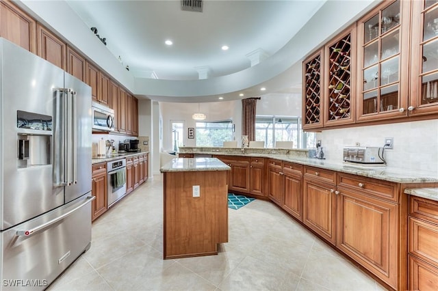 kitchen with a center island, brown cabinets, visible vents, appliances with stainless steel finishes, and light stone countertops